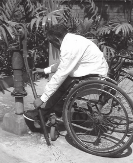 Laki-laki pengguna kursi roda sedang memegang pompa tangan yang ditempatkan pada posisi 90 derajat dari ketinggian kursi roda