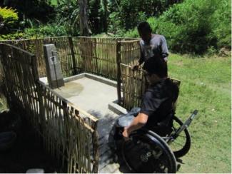 Un homme en fauteuil roulant teste une pompe à eau accessible, en utilisant la rampe jusqu'au tablier.