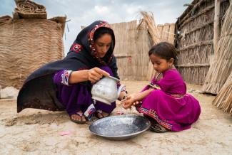 Una mujer ayuda a una niña a lavarse las manos con una jarra de agua
